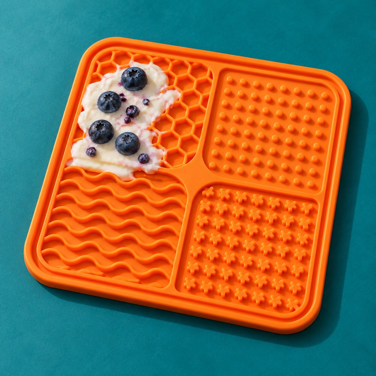 An orange silicone lick mat with yogurt and blueberries